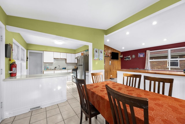 dining space featuring wood walls, lofted ceiling with beams, light tile patterned flooring, and sink