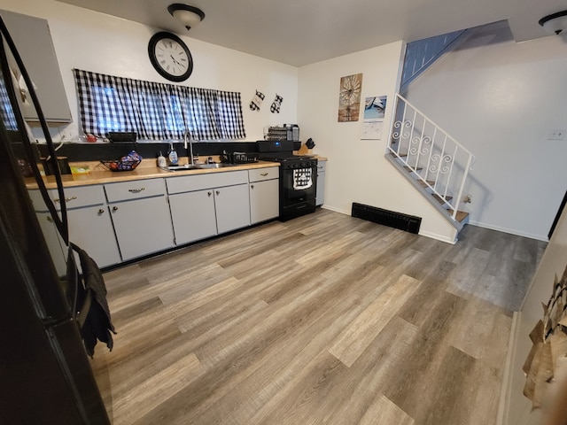 kitchen with sink, light hardwood / wood-style flooring, white cabinets, and black gas range