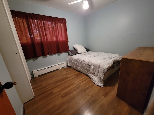 bedroom featuring dark hardwood / wood-style flooring, a baseboard heating unit, and ceiling fan