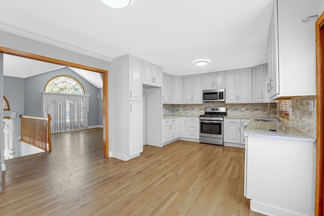 kitchen featuring sink, vaulted ceiling, appliances with stainless steel finishes, light hardwood / wood-style floors, and tasteful backsplash