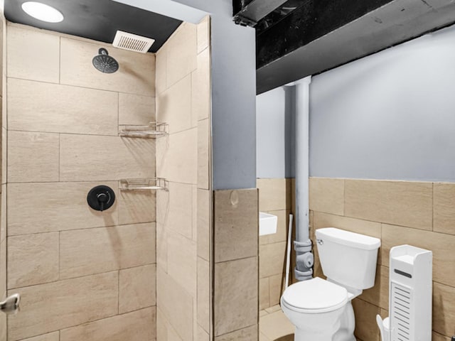 bathroom with tiled shower, toilet, and tile walls