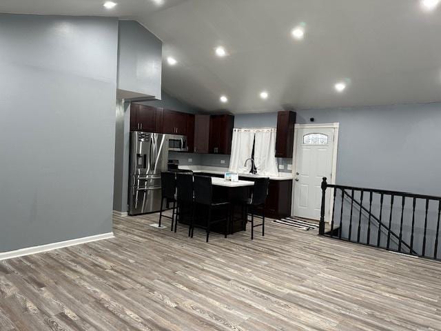 kitchen featuring appliances with stainless steel finishes, lofted ceiling, a kitchen breakfast bar, a center island, and light hardwood / wood-style floors