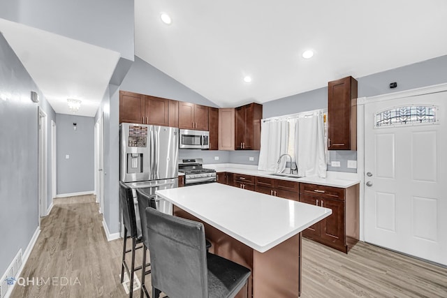 kitchen featuring sink, stainless steel appliances, a center island, light hardwood / wood-style floors, and a kitchen bar