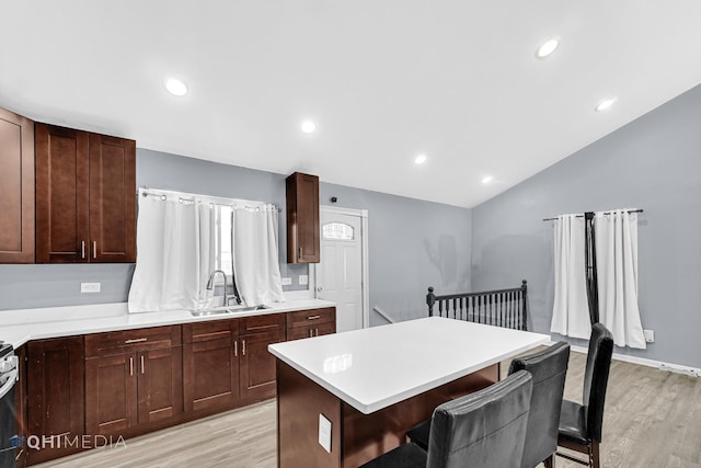 kitchen featuring vaulted ceiling, sink, a kitchen breakfast bar, a center island, and light wood-type flooring