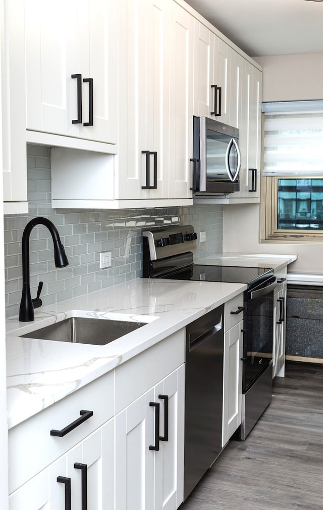 kitchen featuring wood-type flooring, sink, black appliances, white cabinetry, and light stone counters