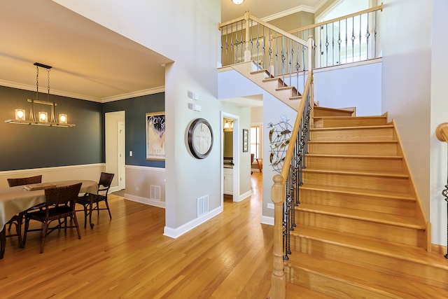 stairway with crown molding, hardwood / wood-style flooring, and an inviting chandelier