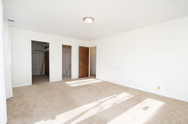 unfurnished bedroom featuring light carpet, a walk in closet, and connected bathroom