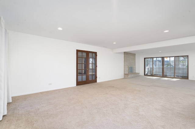 unfurnished room featuring french doors, light colored carpet, and a brick fireplace