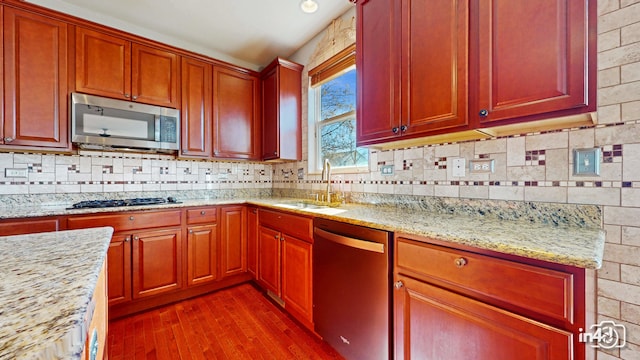 kitchen with light stone counters, backsplash, dark wood-type flooring, sink, and stainless steel appliances