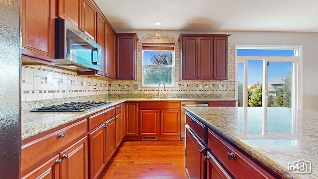 kitchen with light stone countertops, light hardwood / wood-style flooring, appliances with stainless steel finishes, and a wealth of natural light