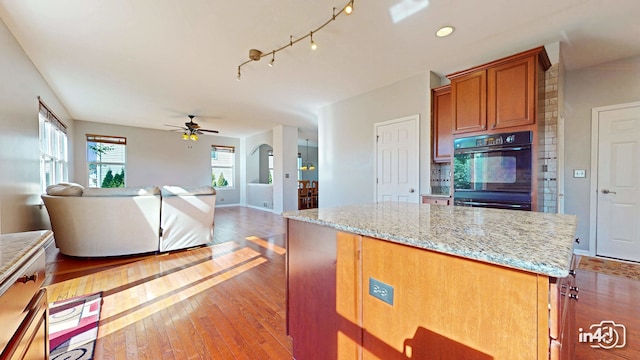 kitchen with ceiling fan, light stone countertops, dark wood-type flooring, double oven, and a center island