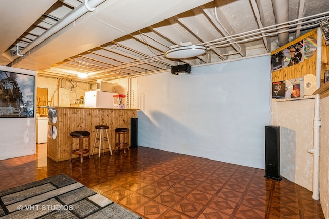 basement featuring bar area, dark parquet floors, and white refrigerator