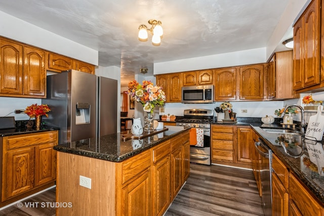 kitchen with appliances with stainless steel finishes, dark hardwood / wood-style flooring, sink, dark stone countertops, and a kitchen island