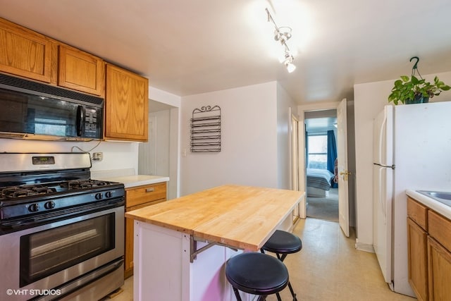 kitchen with gas stove, butcher block countertops, a kitchen island, white refrigerator, and a breakfast bar area