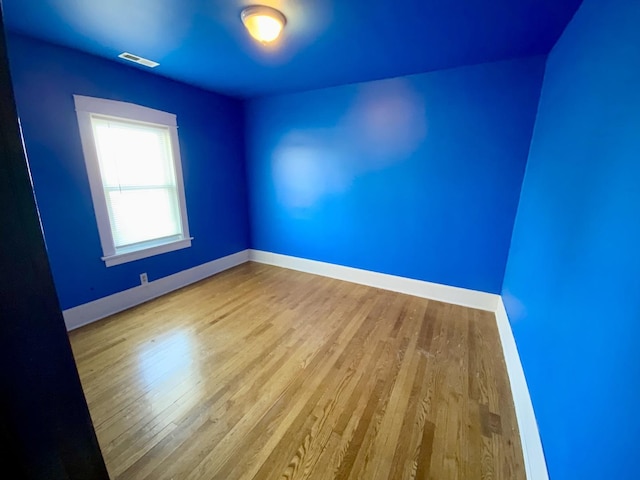 spare room with wood finished floors, visible vents, and baseboards