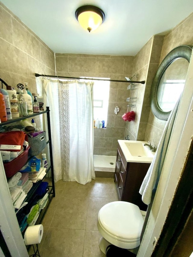 bathroom with tile patterned flooring, toilet, vanity, tile walls, and a stall shower