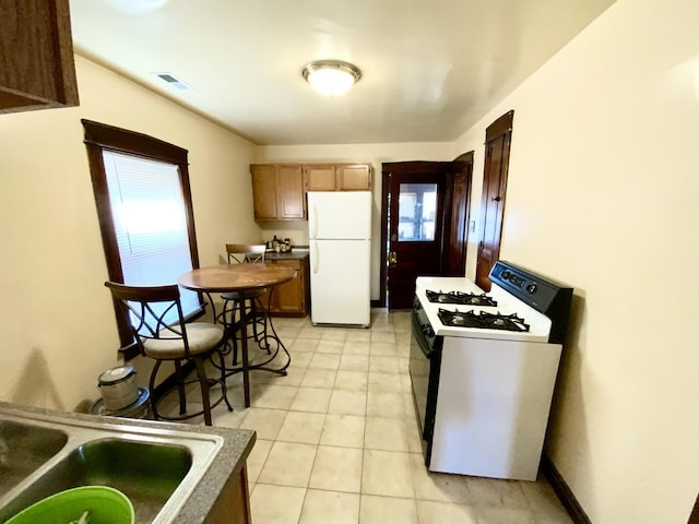 kitchen featuring range with gas cooktop, light tile patterned floors, dark countertops, visible vents, and freestanding refrigerator