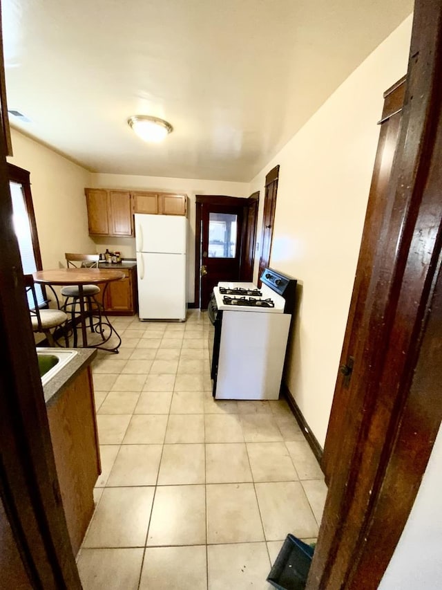 kitchen with white appliances, light tile patterned floors, baseboards, visible vents, and brown cabinets