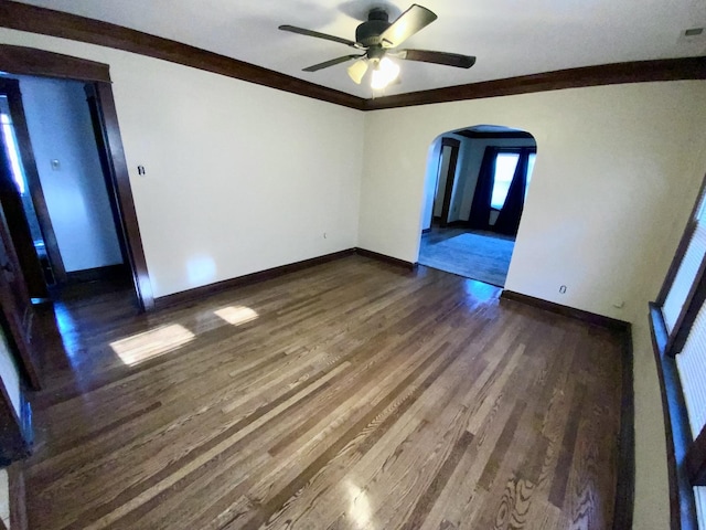 unfurnished room with baseboards, arched walkways, a ceiling fan, dark wood-style floors, and ornamental molding