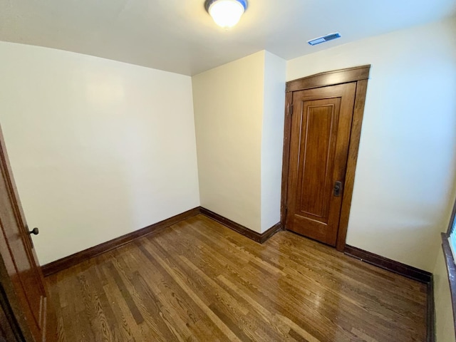 unfurnished room featuring dark wood-style floors, visible vents, and baseboards