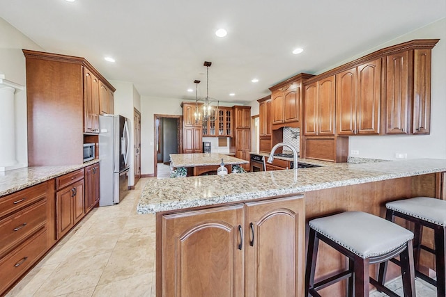 kitchen with appliances with stainless steel finishes, a kitchen bar, light stone countertops, hanging light fixtures, and kitchen peninsula