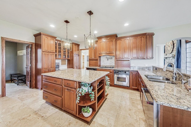 kitchen with a center island, hanging light fixtures, sink, light stone countertops, and appliances with stainless steel finishes