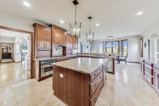 kitchen with kitchen peninsula, appliances with stainless steel finishes, hanging light fixtures, a kitchen island, and ornate columns