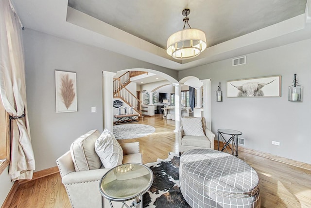 living area featuring a tray ceiling, ornate columns, and light hardwood / wood-style flooring