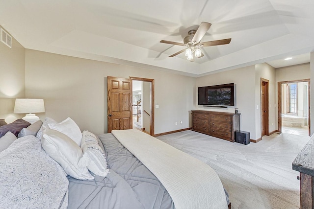 carpeted bedroom with ensuite bath, ceiling fan, and a tray ceiling