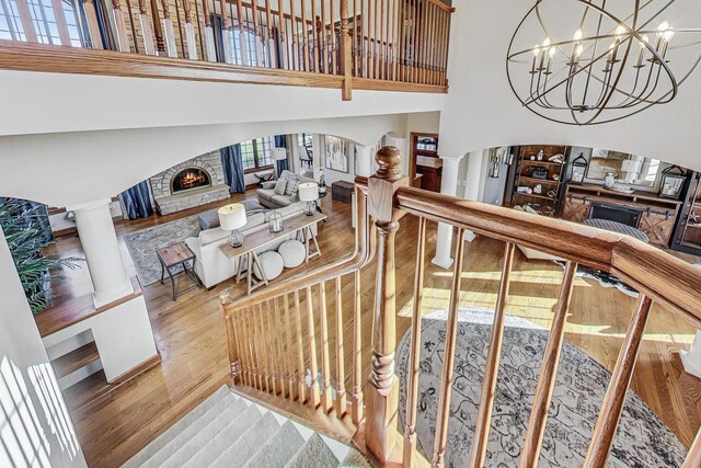 staircase featuring a stone fireplace, hardwood / wood-style floors, ornate columns, and a towering ceiling