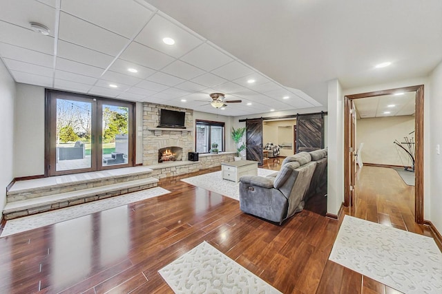 living room featuring a barn door, ceiling fan, wood-type flooring, and a fireplace