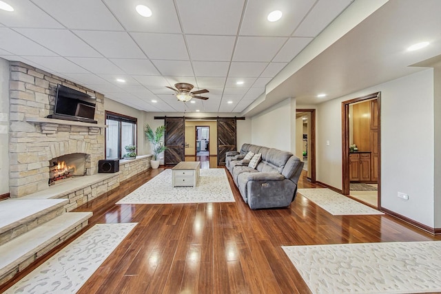 living room with a stone fireplace, hardwood / wood-style floors, a drop ceiling, and a barn door