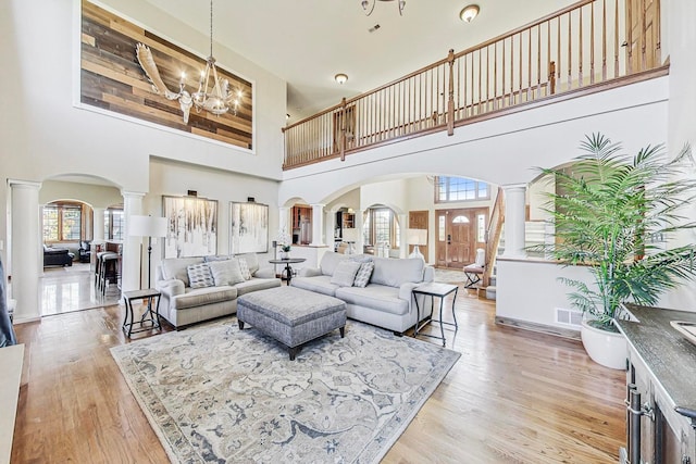 living room featuring light hardwood / wood-style flooring, decorative columns, a chandelier, and a towering ceiling