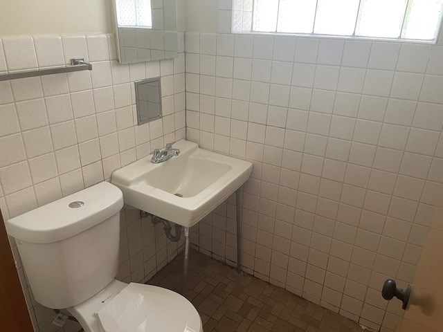 bathroom with toilet, sink, and tile walls