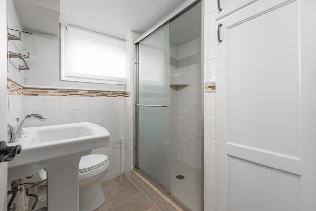 bathroom featuring toilet, tile walls, a shower with shower door, and tile patterned flooring