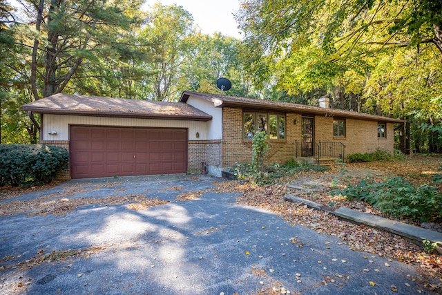 ranch-style home featuring an attached garage, a chimney, aphalt driveway, and brick siding