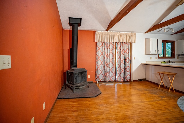 living room with vaulted ceiling with beams, light hardwood / wood-style flooring, a textured ceiling, and a wood stove