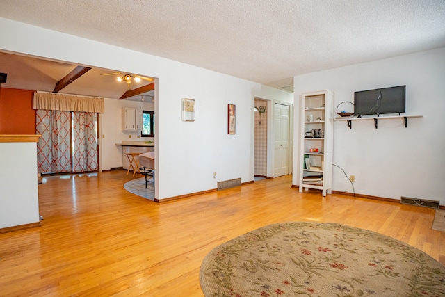 unfurnished living room with hardwood / wood-style floors, a textured ceiling, and beam ceiling