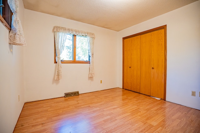 unfurnished bedroom with a closet, light hardwood / wood-style floors, and a textured ceiling