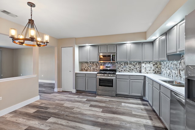 kitchen featuring tasteful backsplash, stainless steel appliances, decorative light fixtures, gray cabinets, and light hardwood / wood-style floors