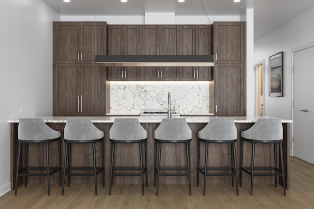 kitchen with a kitchen breakfast bar, a center island with sink, and hardwood / wood-style flooring