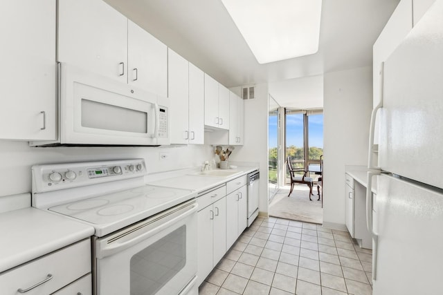 kitchen featuring white appliances, white cabinets, light tile patterned flooring, expansive windows, and sink