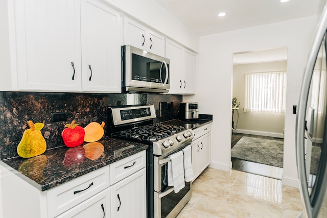 kitchen with white cabinets, dark stone countertops, stainless steel appliances, and backsplash