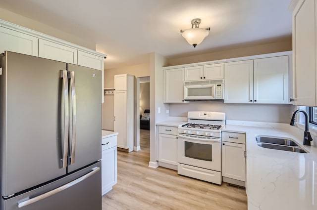 kitchen with sink, white cabinetry, white appliances, and light hardwood / wood-style floors