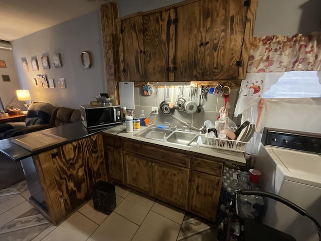 kitchen with washer / dryer, dark brown cabinetry, light tile patterned floors, and sink