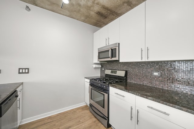 kitchen with appliances with stainless steel finishes, white cabinetry, dark stone countertops, decorative backsplash, and light hardwood / wood-style flooring