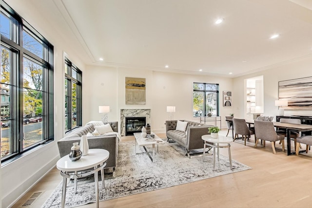 living room featuring a high end fireplace, light hardwood / wood-style flooring, and crown molding