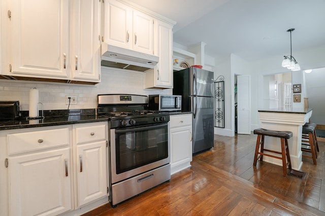 kitchen with decorative backsplash, dark wood-type flooring, hanging light fixtures, white cabinetry, and appliances with stainless steel finishes