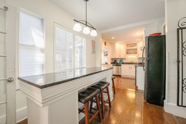 kitchen with white cabinets, dark hardwood / wood-style flooring, appliances with stainless steel finishes, a kitchen bar, and pendant lighting