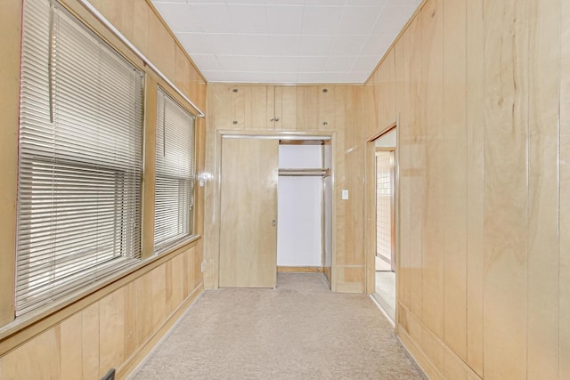 hallway featuring light carpet and wooden walls